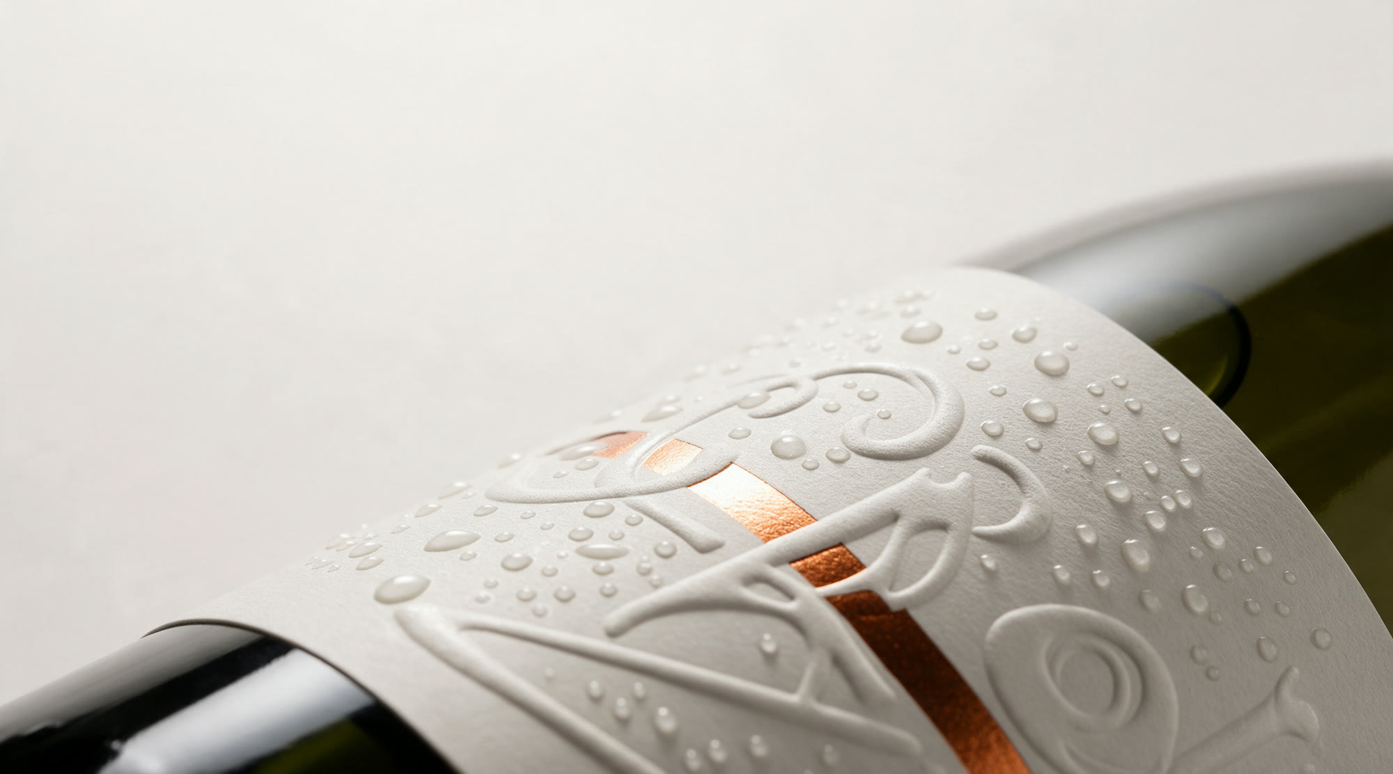 Close-up of a label corner showing raised clear varnish, sculpted embossing and a stripe of copper foil