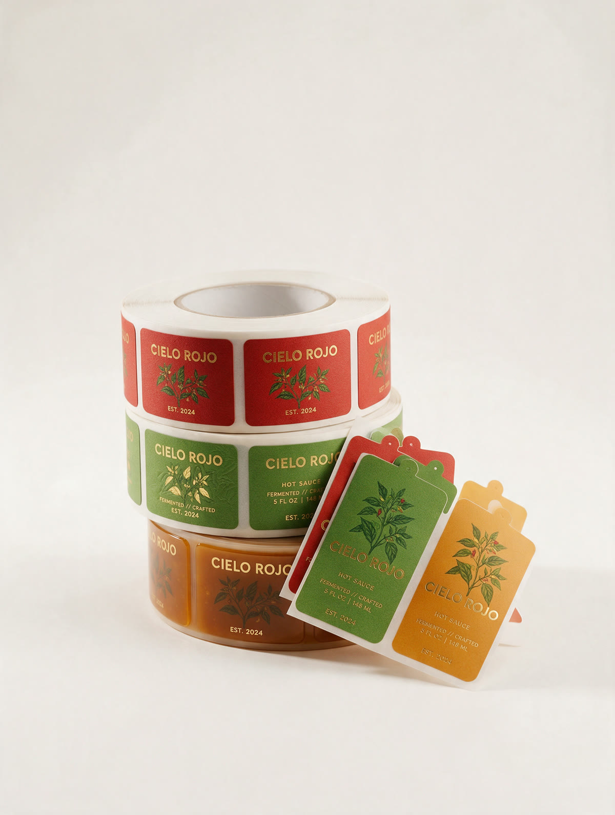 Three rolls of Cielo Rojo hot sauce labels in red, green and amber colourways, with loose die-cut labels beside them